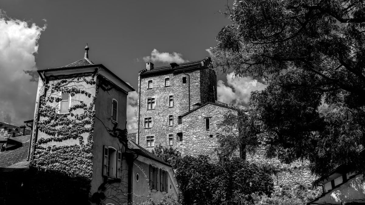 Black and white photo of a historic castle with ivy-covered walls in Switzerland.